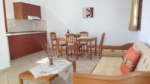 A compact living space with a kitchenette, a dining area with wooden chairs, and a sofa with cushions. - Golden Sun (Karpathos)