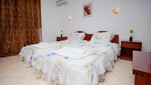 A double bed with floral bedding, two bedside tables, a wall-mounted air conditioner, and a red flower decoration. - Golden Sun (Karpathos)
