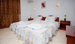 A double bed with floral bedding, two bedside tables, a wall-mounted air conditioner, and a red flower decoration. - Golden Sun (Karpathos)