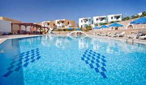 A swimming pool with clear blue water, lounge chairs, and a covered seating area. - Golden Sun (Karpathos)