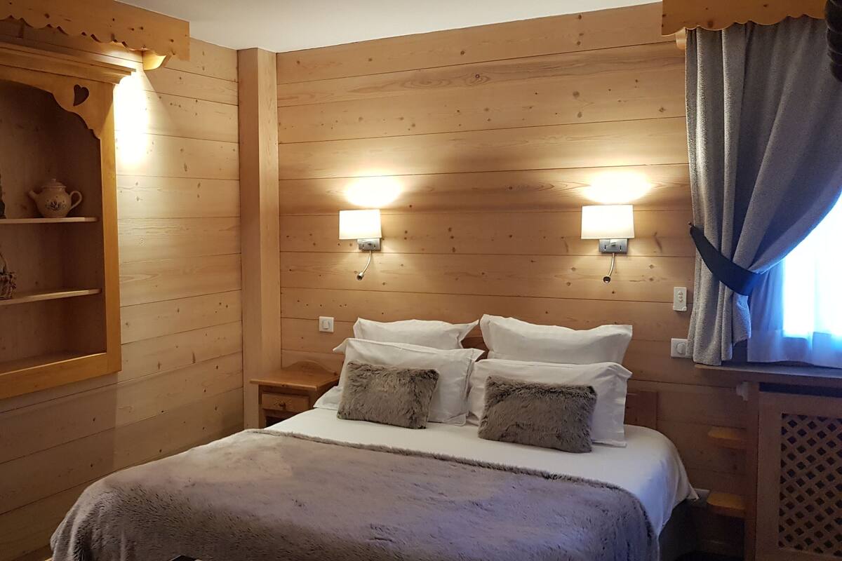A wooden cabin-style room with a bed, two bedside tables, a shelf with decorative items, and wall-mounted lights.