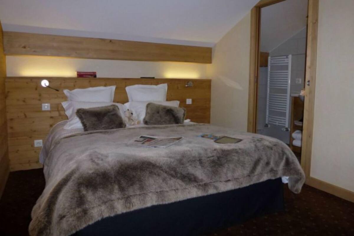 A bedroom with a wooden headboard, a bed with a fur throw, and a mirror in the corner.