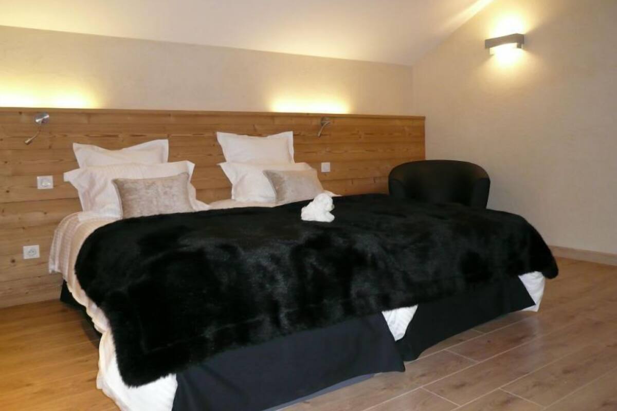 A bedroom with a wooden headboard, a black fur throw, and a black chair.