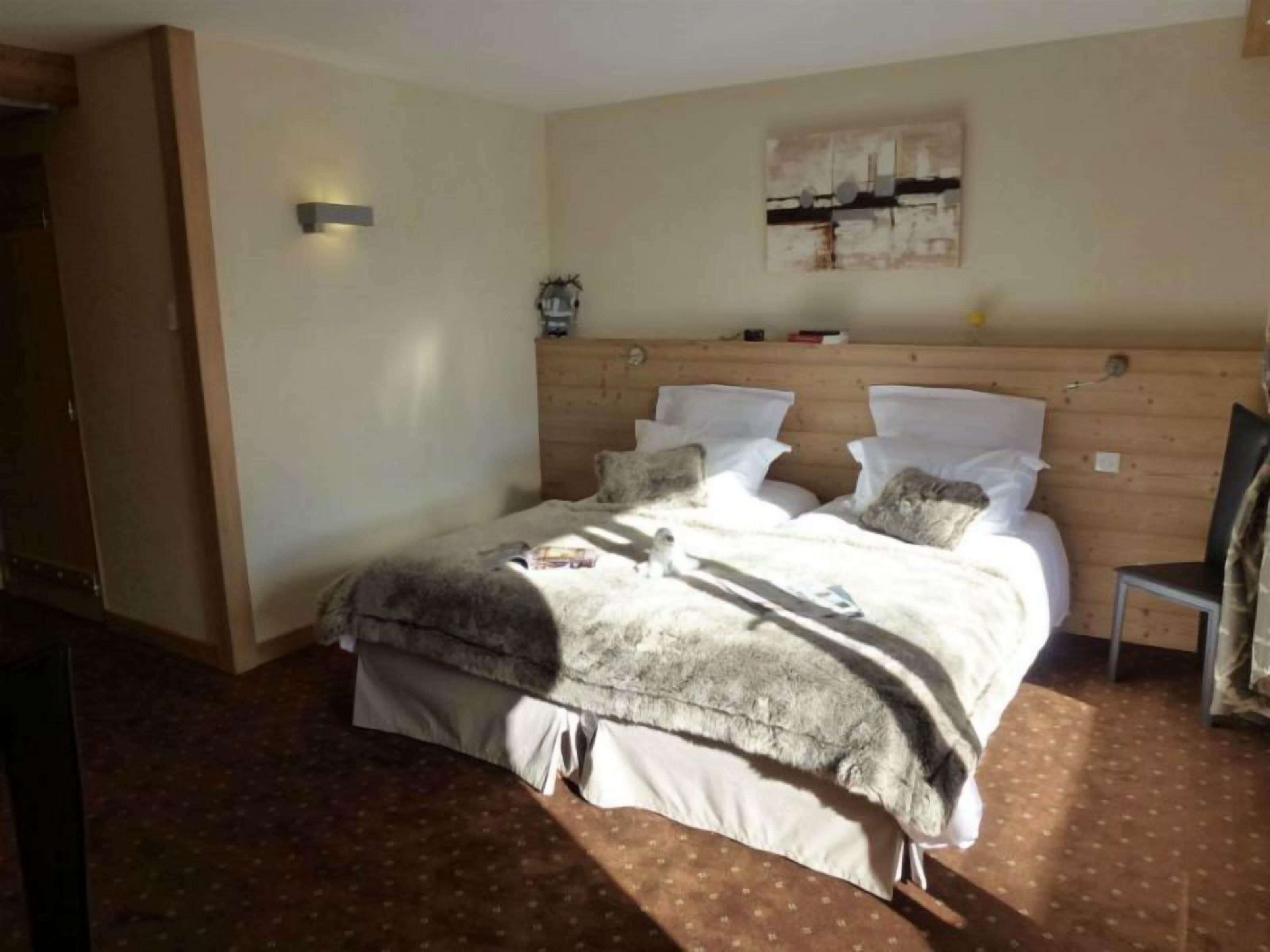 Een slaapkamer met een houten hoofdbord, een bed met witte lakens, een klein nachtkastje en een wandlamp.