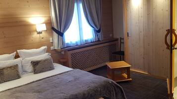 Una habitación con paneles de madera, una cama, un taburete pequeño y una ventana con cortinas.