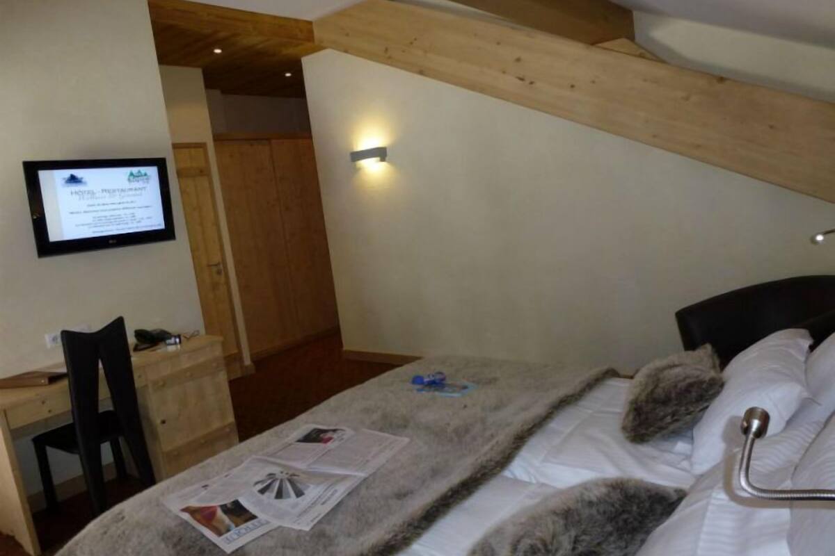 A bedroom with a bed, a desk, a chair, and a wall-mounted TV.