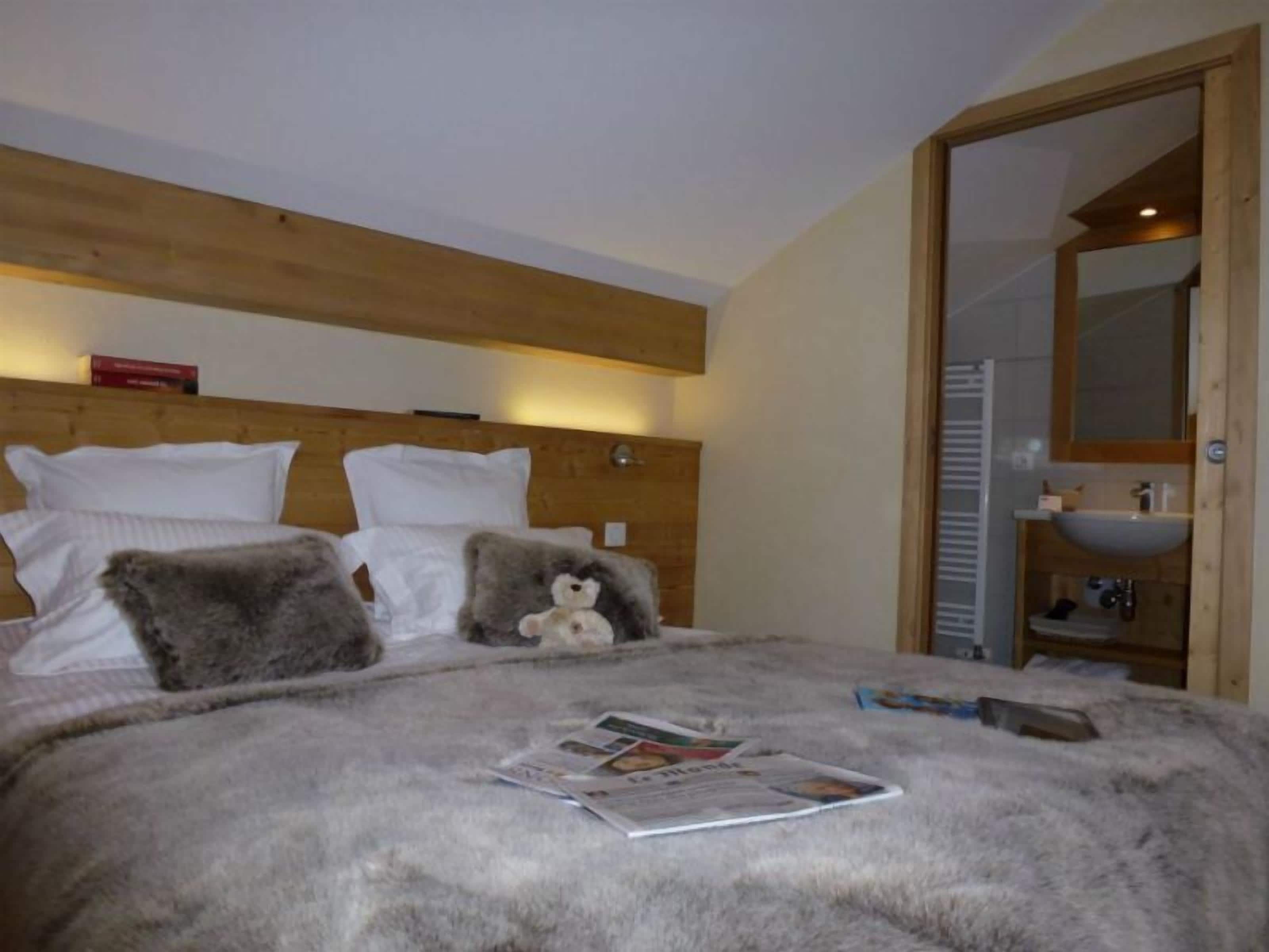 Un dormitorio con cabecera de madera, una cama con almohadas blancas y grises, un osito de peluche y una revista sobre la cama.