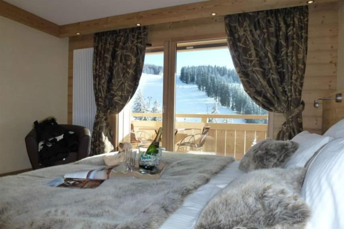 A bedroom with a large bed, a wooden headboard, a window with curtains, and a view of a snowy landscape.