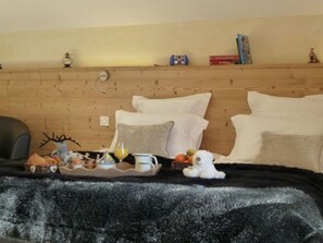 A cozy room with a wooden headboard, a plush black blanket, a tray with snacks, a stuffed toy, and a small lamp. - Hôtel Restaurant Les Sapins Wellness & Gourmet (Manigod)