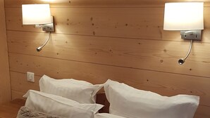 A bedroom with a wooden headboard, two wall-mounted lights, a white bed with fluffy pillows, and a white blanket. - Hôtel Restaurant Les Sapins Wellness & Gourmet (Manigod)