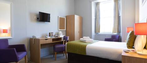 A hotel room with a bed, desk, chairs, a television, and a window with curtains.