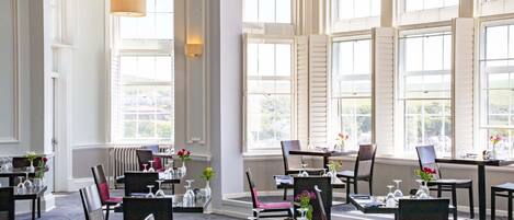 Un comedor amplio con varias mesas y sillas, ventanas grandes y vistas al exterior.