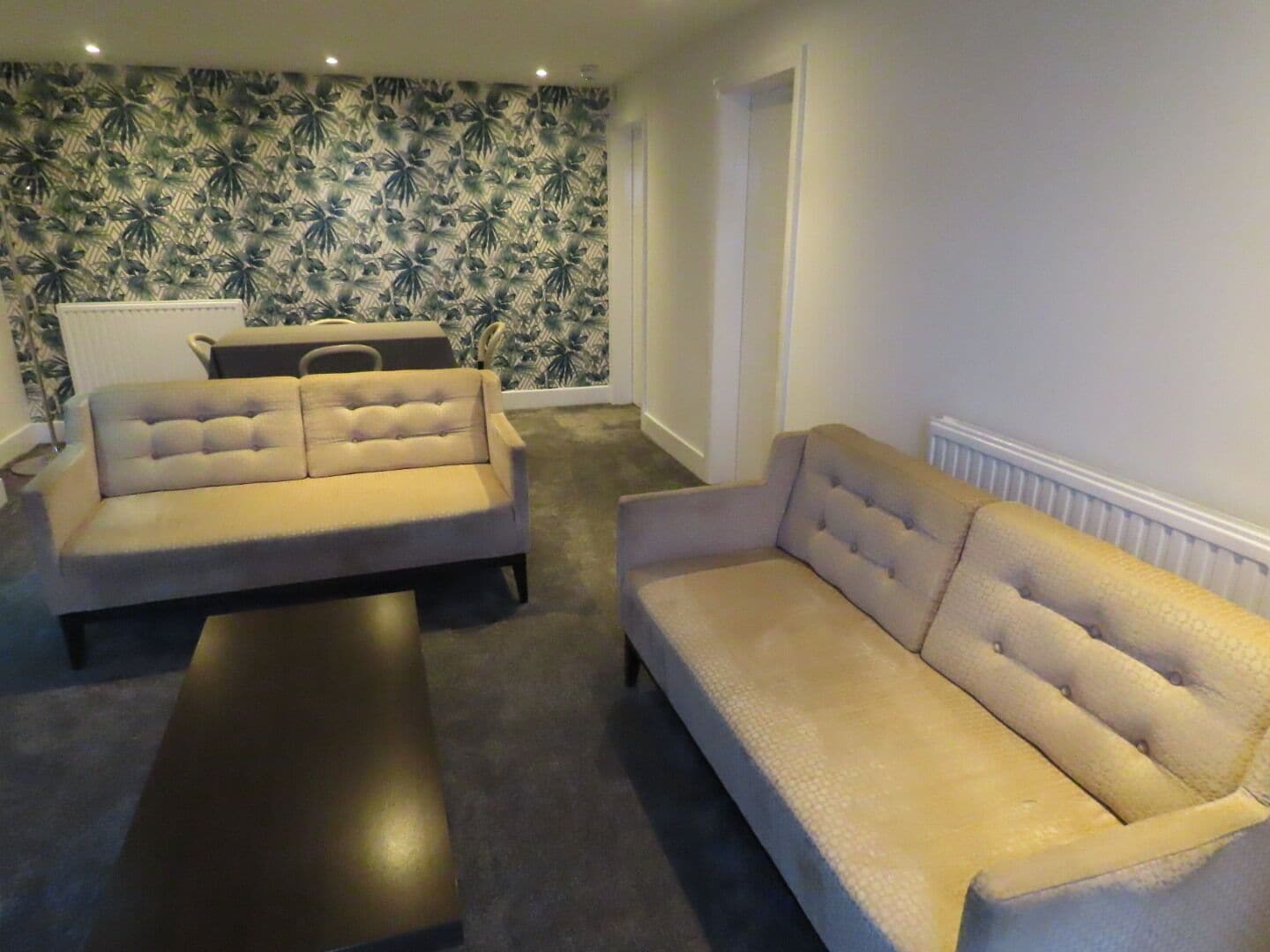 A living room with two sofas and a coffee table, a patterned wallpaper, and a radiator on the wall.