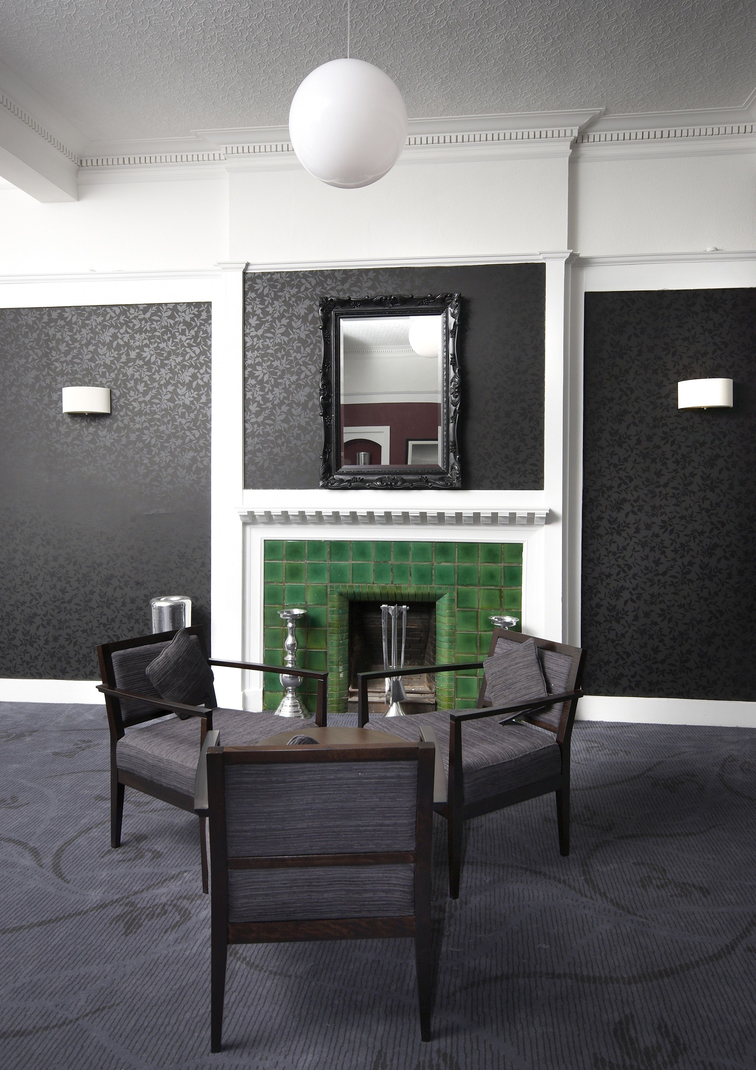 A room with a fireplace, two armchairs, a table, and a hanging light fixture.
