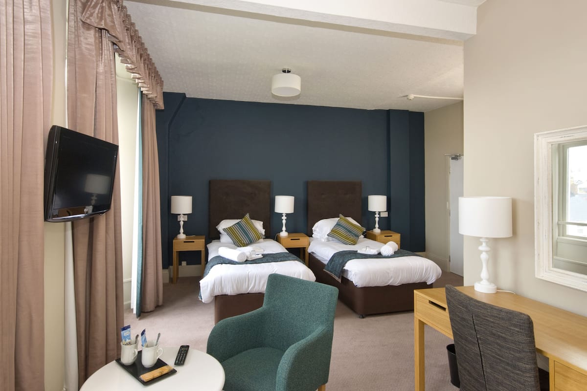 A hotel room with two beds, a TV mounted on the wall, a desk with a chair, and a window.