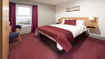 A hotel room with a large bed, a desk with a chair, a window with curtains, and a painting on the wall.