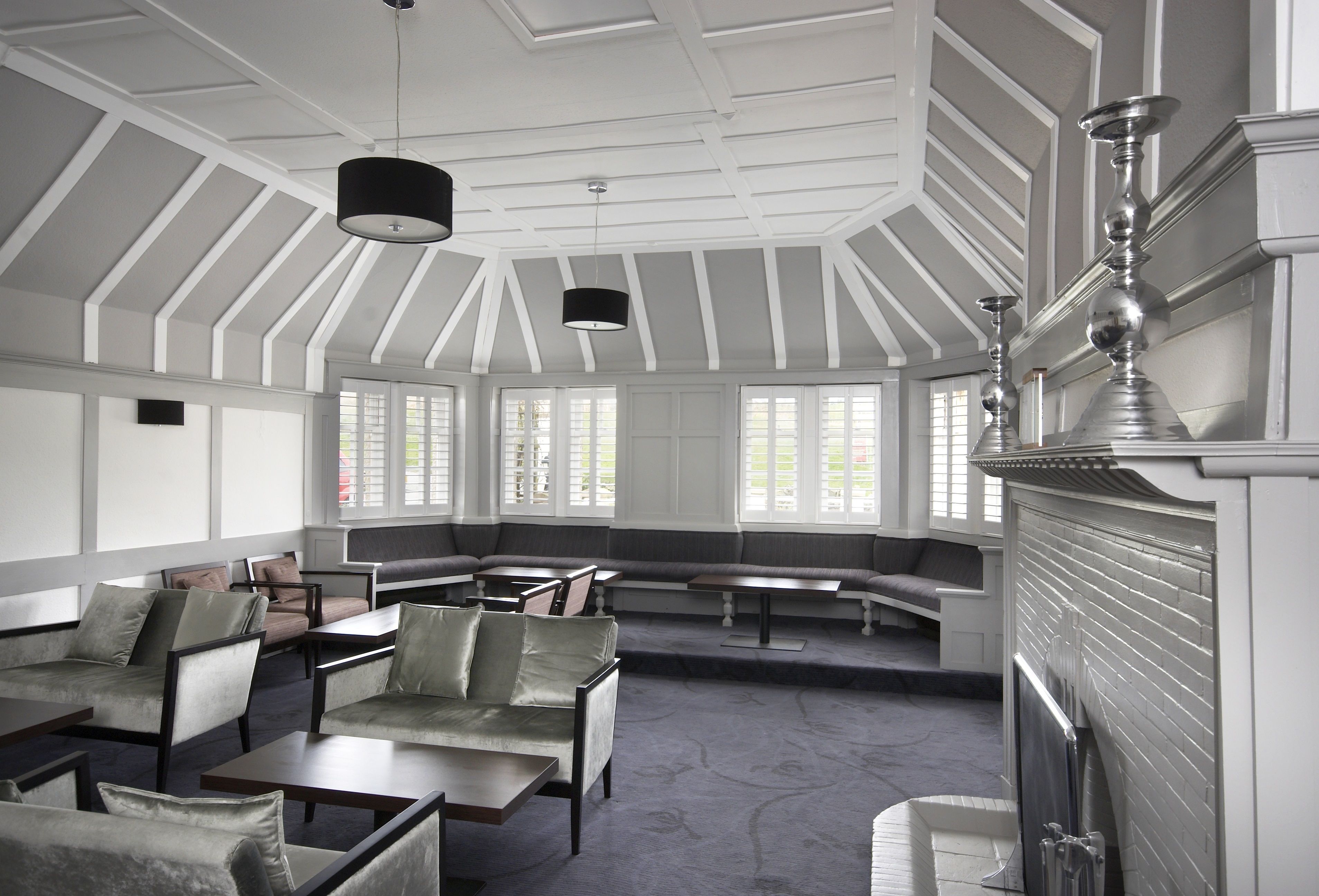 Une pièce spacieuse avec un plafond haut, de grandes fenêtres et une cheminée. On y trouve plusieurs coins salon avec des canapés et des tables.