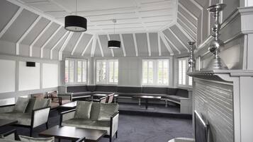Une pièce spacieuse avec un plafond haut, de grandes fenêtres et une cheminée. On y trouve plusieurs coins salon avec des canapés et des tables.