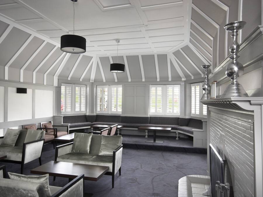 Une pièce spacieuse avec un plafond haut, de grandes fenêtres et une cheminée. On y trouve plusieurs coins salon avec des canapés et des tables.