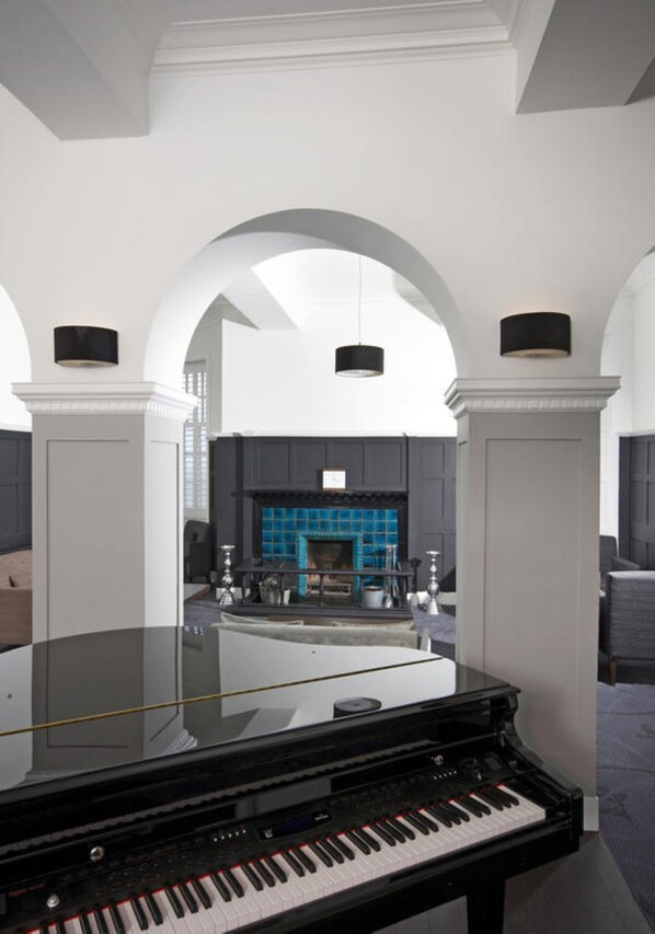 Un piano de cola imponente en una habitación amplia con paredes blancas y arcos, una chimenea y una pared de azulejos azules.