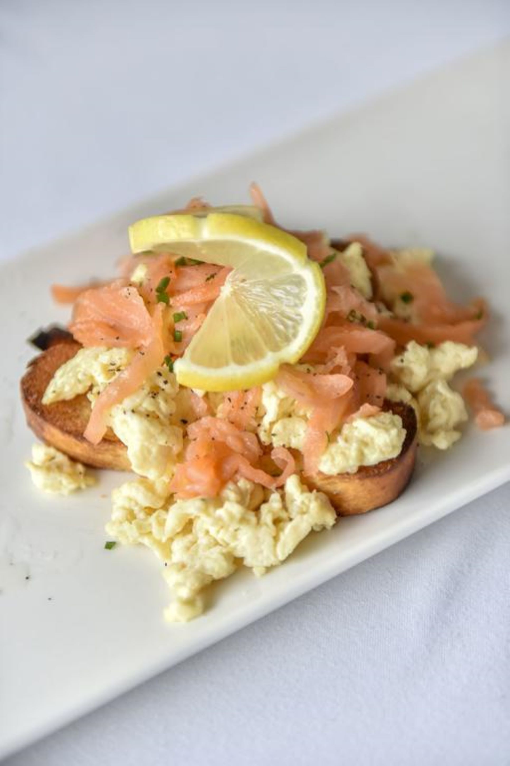 A dish with scrambled eggs, smoked salmon, and a lemon wedge on toast.