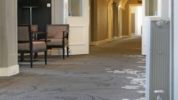 Pasillo de hotel con alfombra estampada, mostrador de recepción y señalización que indica la ubicación de habitaciones y baños.