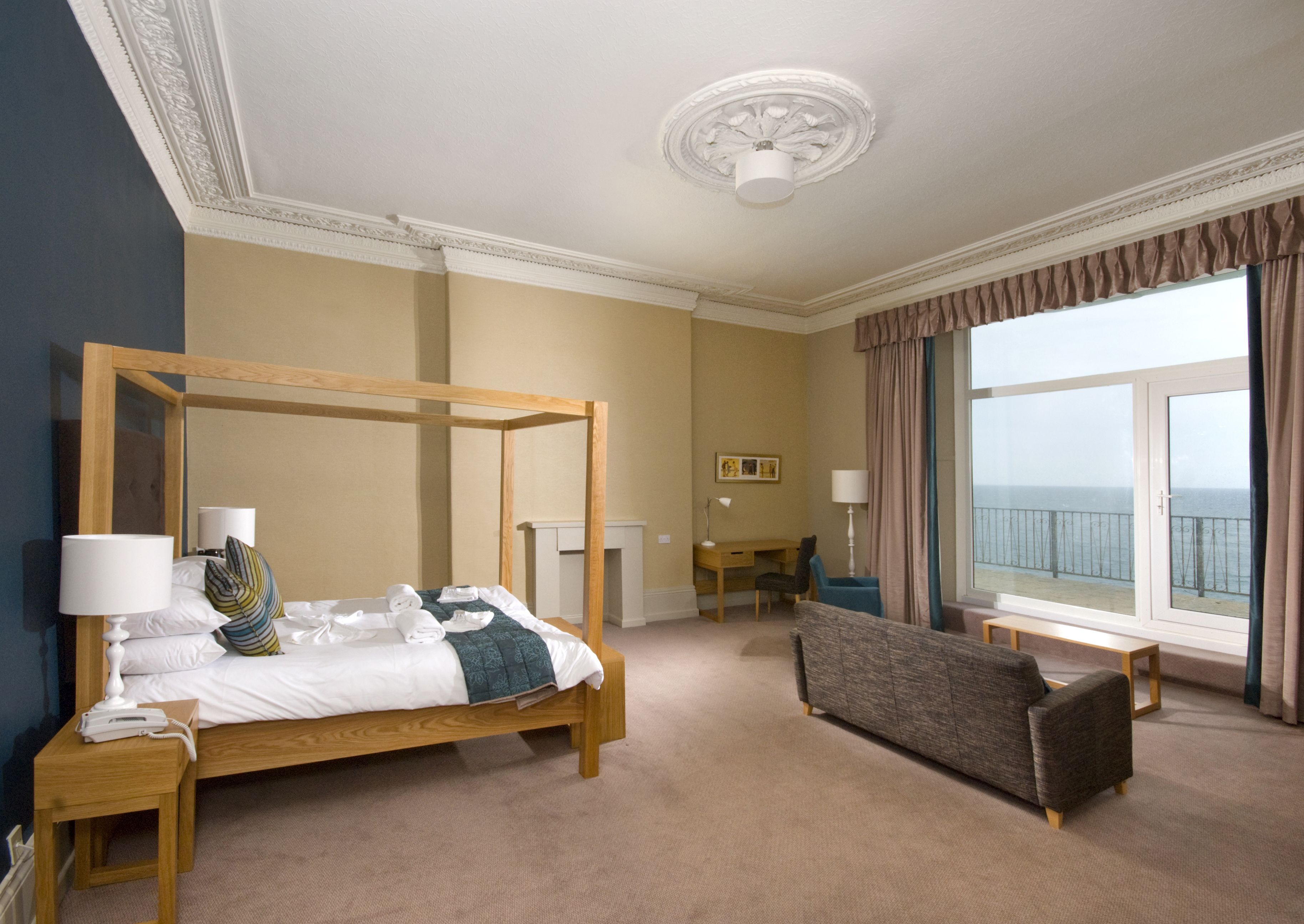 A hotel room with a four-poster bed, a sofa, a desk, and a view of the sea.