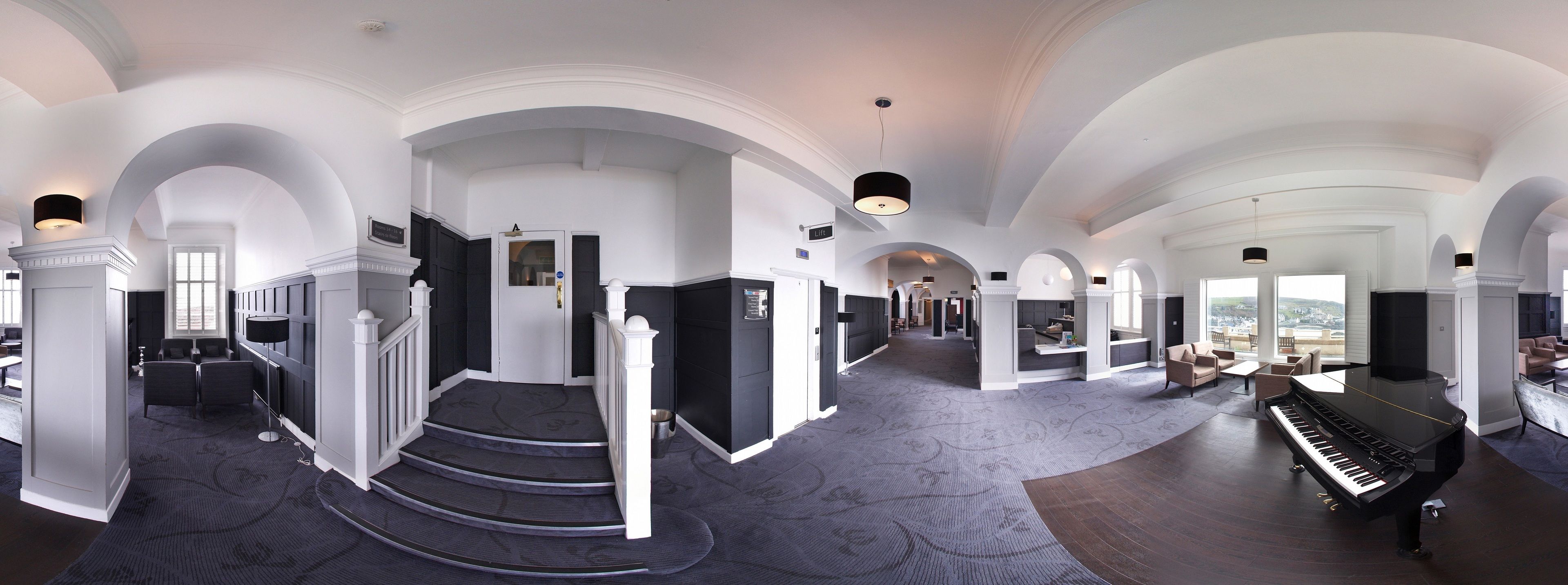 A grand hotel lobby with a grand piano, a staircase, and a view of the city.
