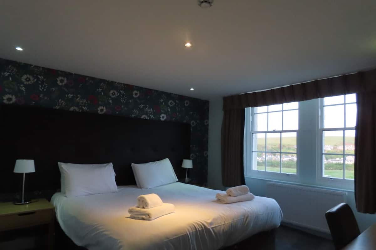 A hotel room with a large bed, two bedside tables, a window with curtains, and a floral wallpaper design.