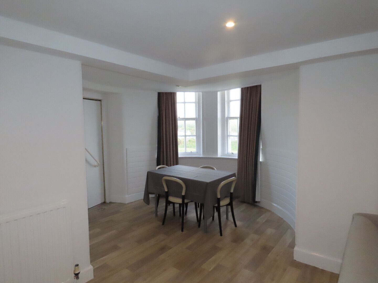 Uma sala de jantar com mesa, cadeiras, janelas amplas e decoração em tons de branco.