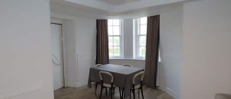 Uma sala de jantar com mesa, cadeiras, janelas amplas e decoração em tons de branco.