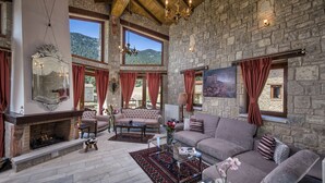 Un salon spacieux aux murs en pierre, doté d’une cheminée et d’une grande fenêtre offrant une vue sur les montagnes.