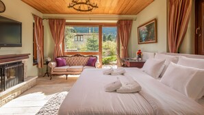Une chambre à coucher avec un grand lit, une cheminée, un téléviseur et une vue sur l’extérieur.