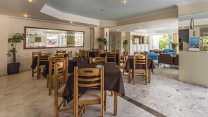 A dining area with wooden chairs and tables, a large mirror on the wall, and a view of the outdoor seating area. - Sunshine (Zakynthos)