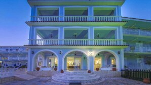 A two-story building with a balcony on the upper floor, a covered entrance with arches, and a stone-paved courtyard. - Sunshine (Zakynthos)