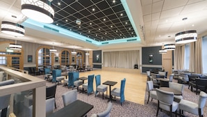 Un amplio vestíbulo de hotel con un escenario, varias zonas de descanso e iluminación moderna.
