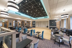 A spacious hotel lobby with a stage, multiple seating areas, and modern lighting fixtures.