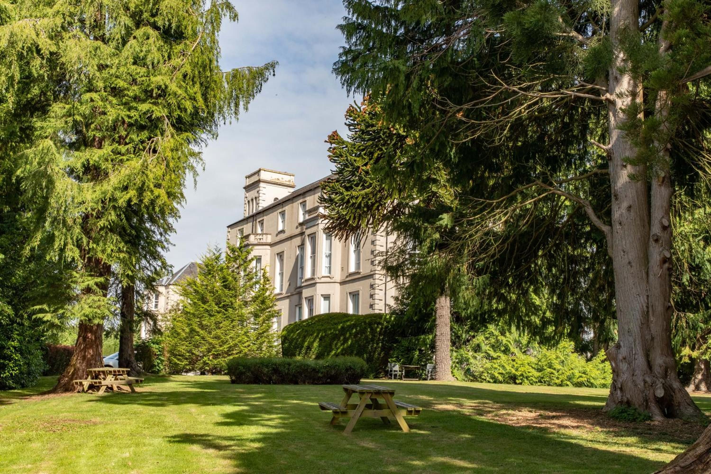 A large building surrounded by lush greenery and a picnic table in a well-maintained lawn.