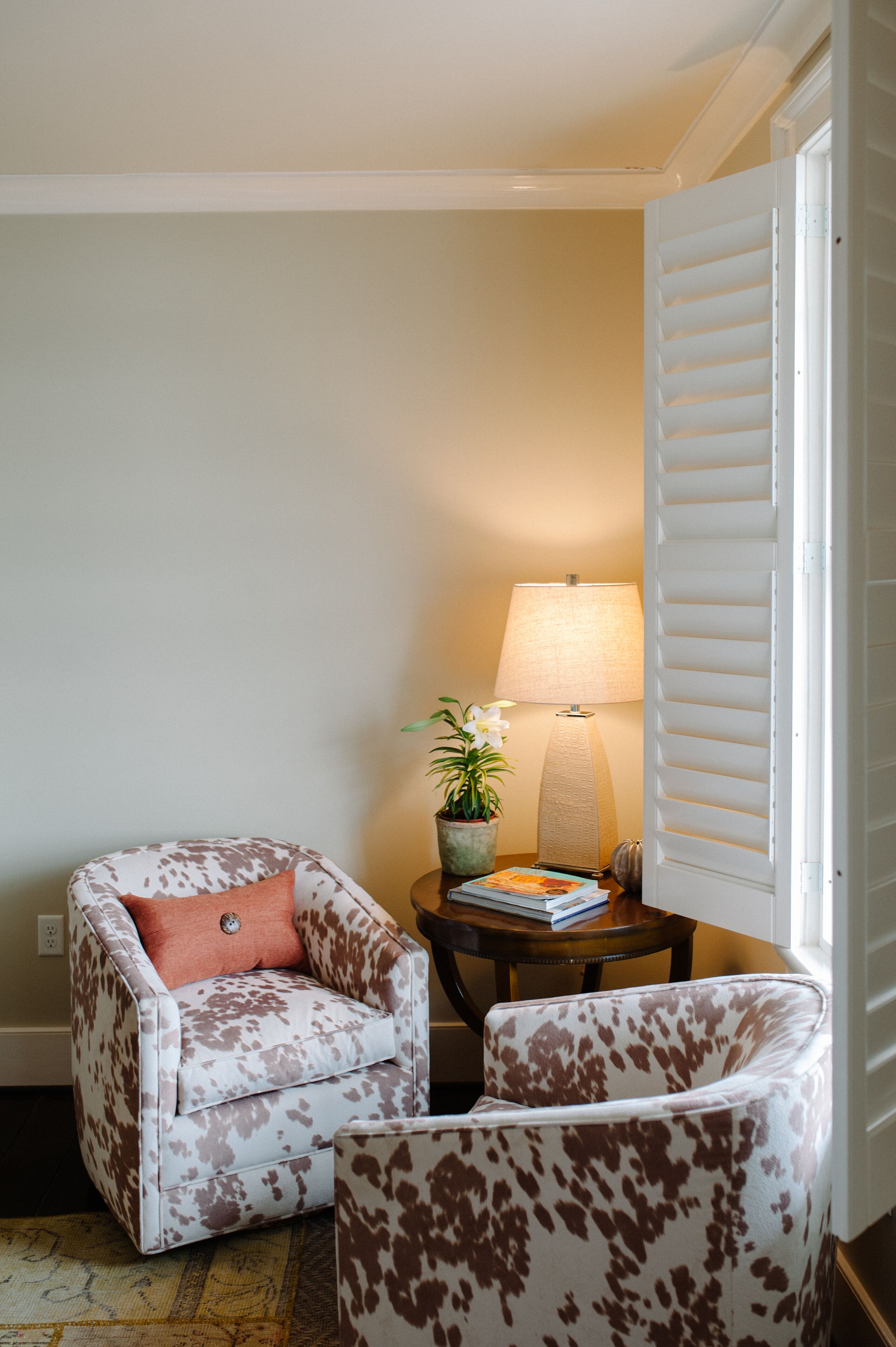 Un rincón acogedor con un sillón estampado, una mesita auxiliar con lámpara y una planta en maceta.