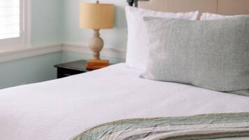 A neatly made bed with a headboard, a bedside lamp, and a window with blinds.