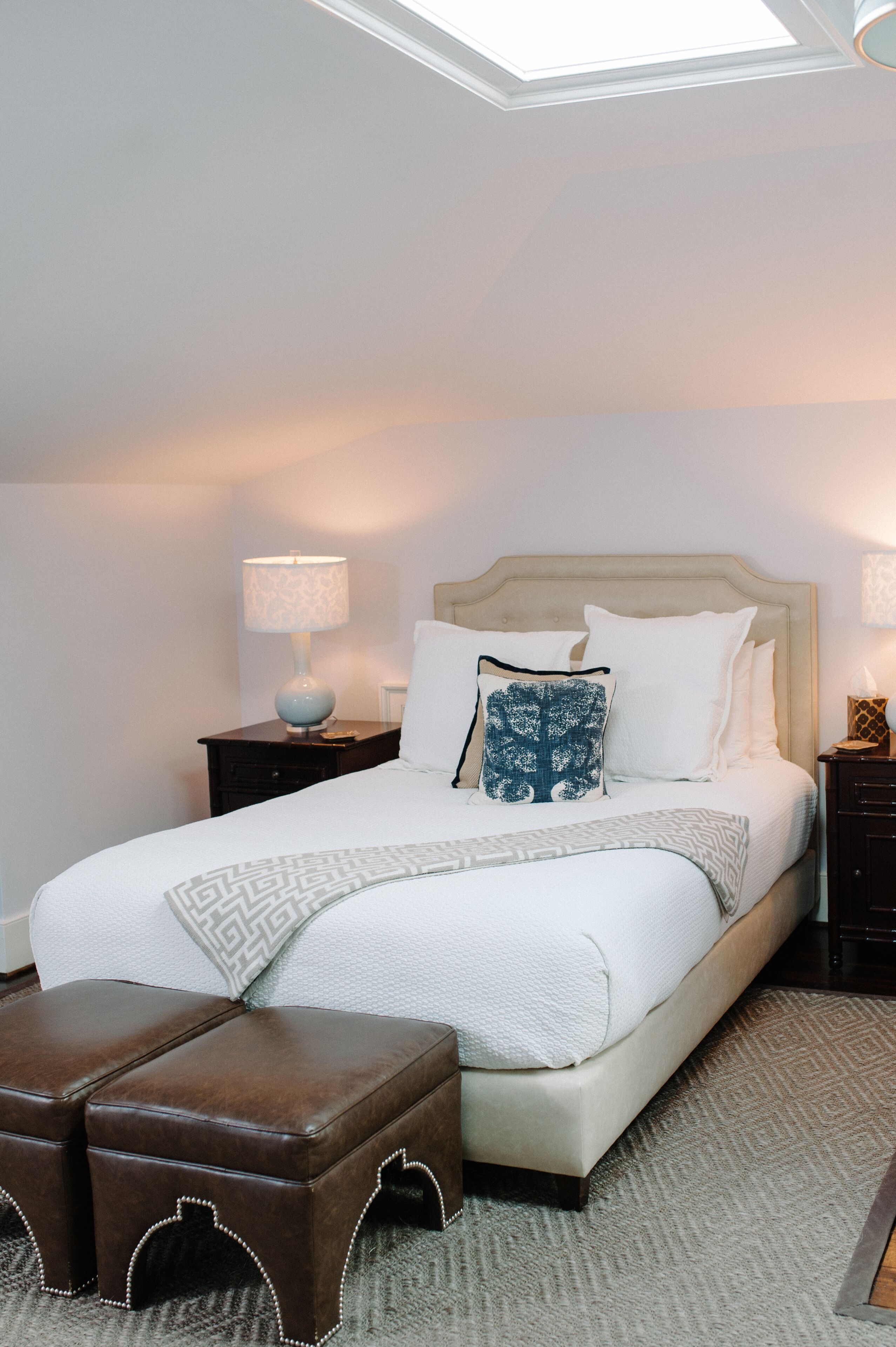 A neatly made bed with a headboard, two bedside tables, and a small ottoman.