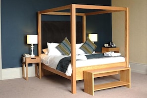 A four-poster bed with a wooden frame, two bedside tables with lamps, and a bedside shelf.
