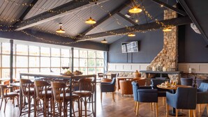 Un restaurante con taburetes de madera, mesas redondas e iluminación colgante con guirnaldas.
