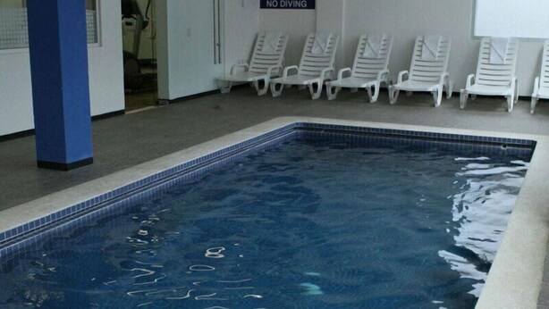 Piscina interna com cadeiras de descanso brancas e aviso proibindo saltos.