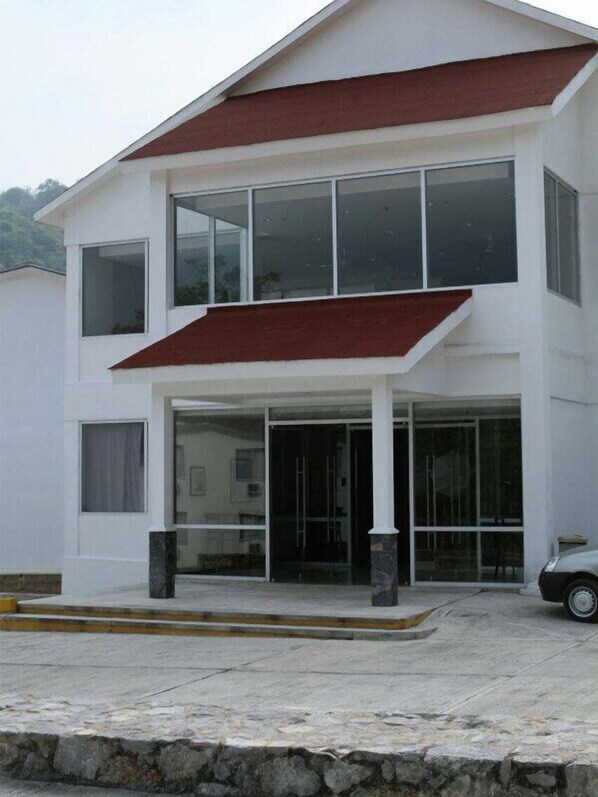 Una casa de dos pisos con techo rojo, ventanas grandes y base de piedra.
