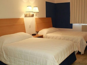 Habitación de hotel con dos camas, cabecero de madera, mesita de noche y lámpara de pared.