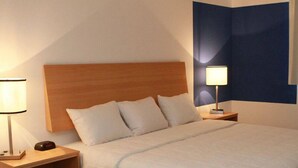 Uma cama bem arrumada com cabeceira de madeira, mesa de cabeceira com abajur e prateleira na parede.