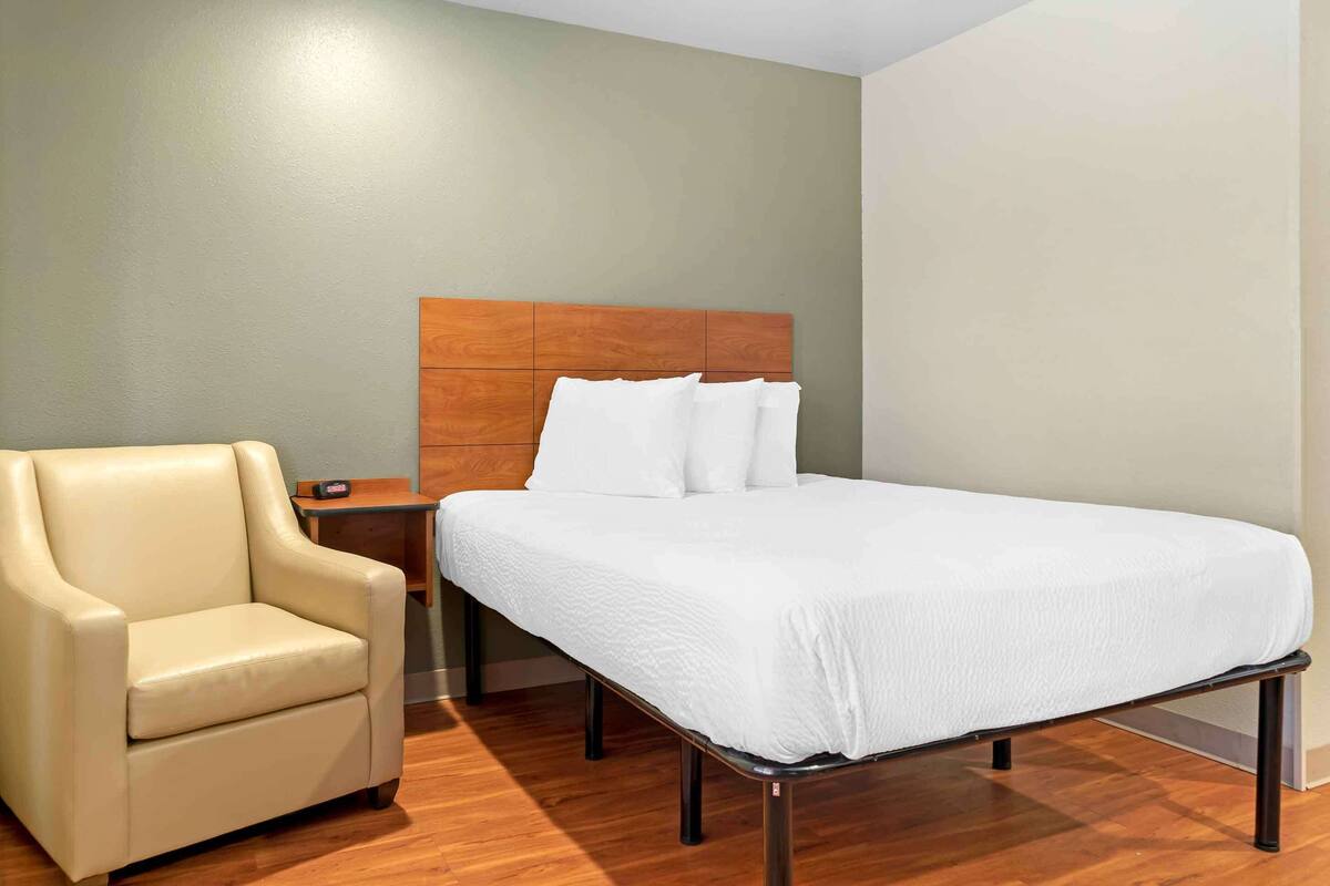 A hotel room with a bed, a chair, and a nightstand.
