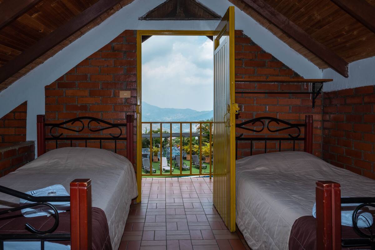 A room with two beds, a balcony, and a view of the mountains.