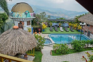 A pool area with lounge chairs, a thatched-roof structure, and a view of distant mountains. - Ecovilla (Cali)